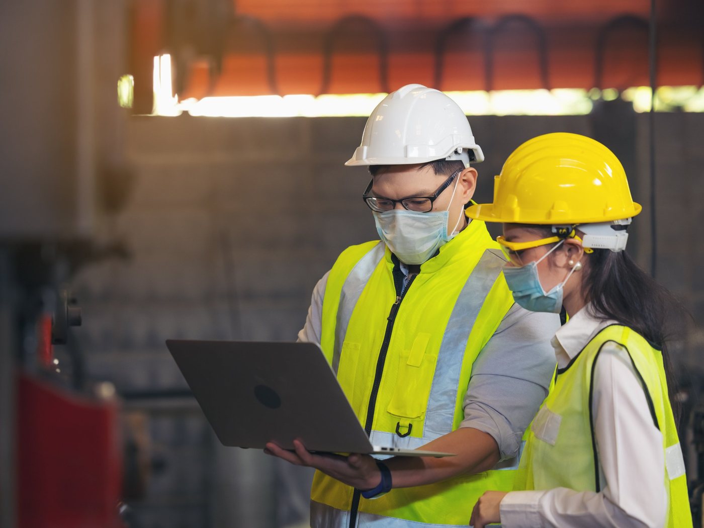 Dos profesionales de seguridad industrial con casco revisan información en un portátil dentro de una planta